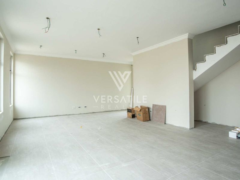 An open-plan living area in a townhouse, featuring neutral tiled flooring, a staircase, and unfinished electrical points, presenting a blank canvas for interior design.