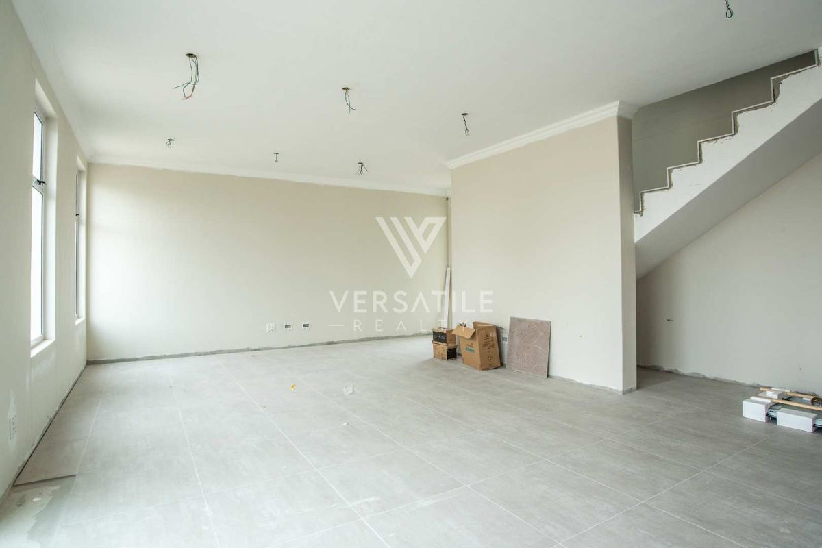 An open-plan living area in a townhouse, featuring neutral tiled flooring, a staircase, and unfinished electrical points, presenting a blank canvas for interior design.