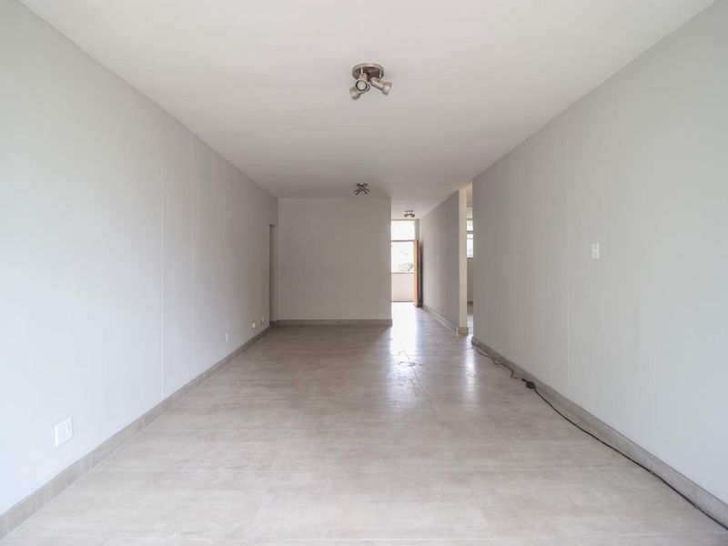 A spacious, empty living area featuring neutral tiled flooring and modern spotlight fixtures, offering a clean and versatile blank canvas.