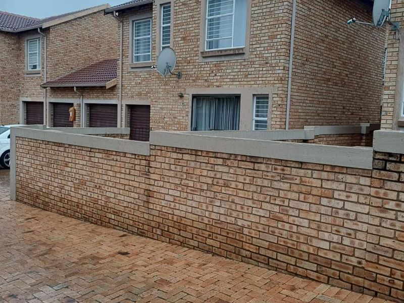 A view of the front exterior of a face-brick cluster home featuring a paved driveway, boundary wall, and integrated garage doors.