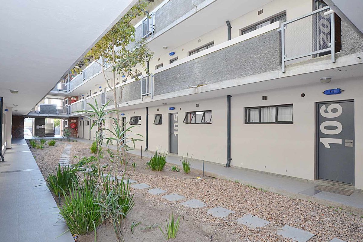 Exterior view of an apartment complex featuring a covered walkway, gravel courtyard, and multiple unit entrances with metal railings.