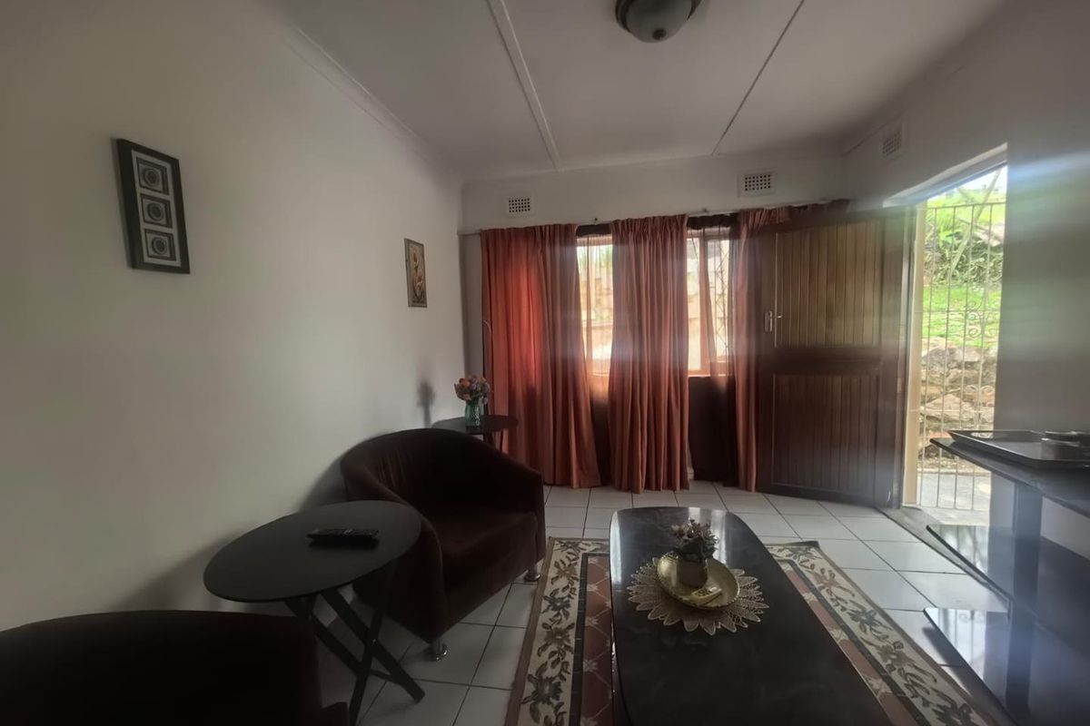 A living room featuring tiled flooring, a ceiling light fixture, and direct access to the exterior through a timber door with a security gate.