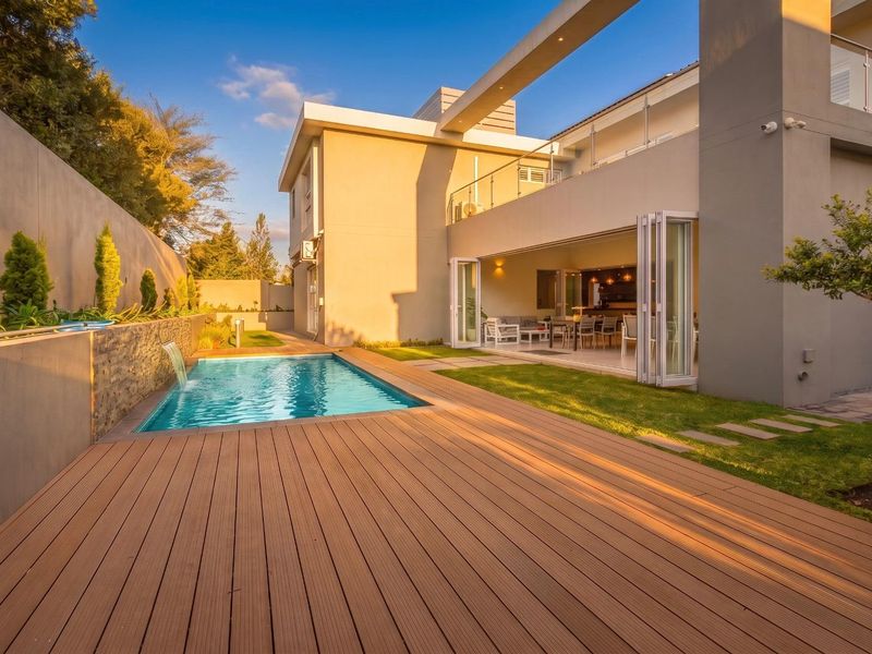 Modern outdoor entertainment area featuring a swimming pool with water feature, timber decking, and seamless indoor-outdoor flow through large stacking glass doors.