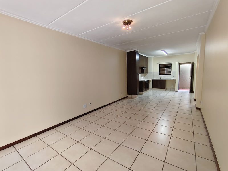 An open-plan living and kitchen area featuring neutral tiled flooring, built-in dark cabinetry, and a functional kitchen layout.
