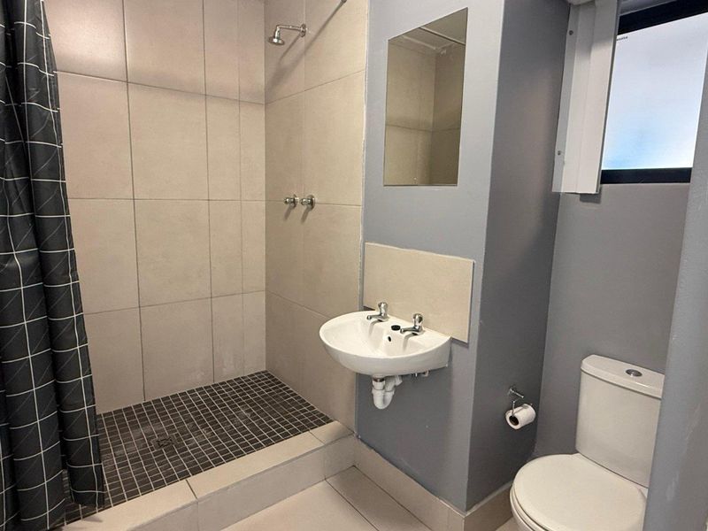 A functional bathroom featuring a walk-in shower with tiled surround, a wall-mounted basin, and a standard toilet.