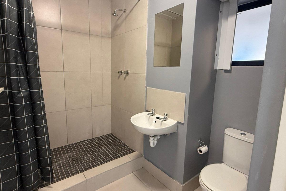 A functional bathroom featuring a walk-in shower with tiled surround, a wall-mounted basin, and a standard toilet.