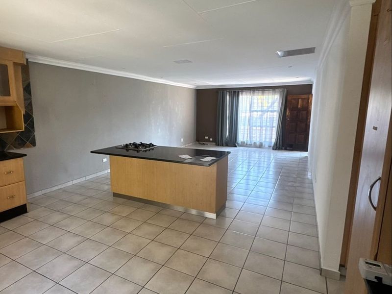 Spacious open-plan living area featuring a central kitchen island with a gas hob, tiled flooring throughout, and neutral wall finishes.