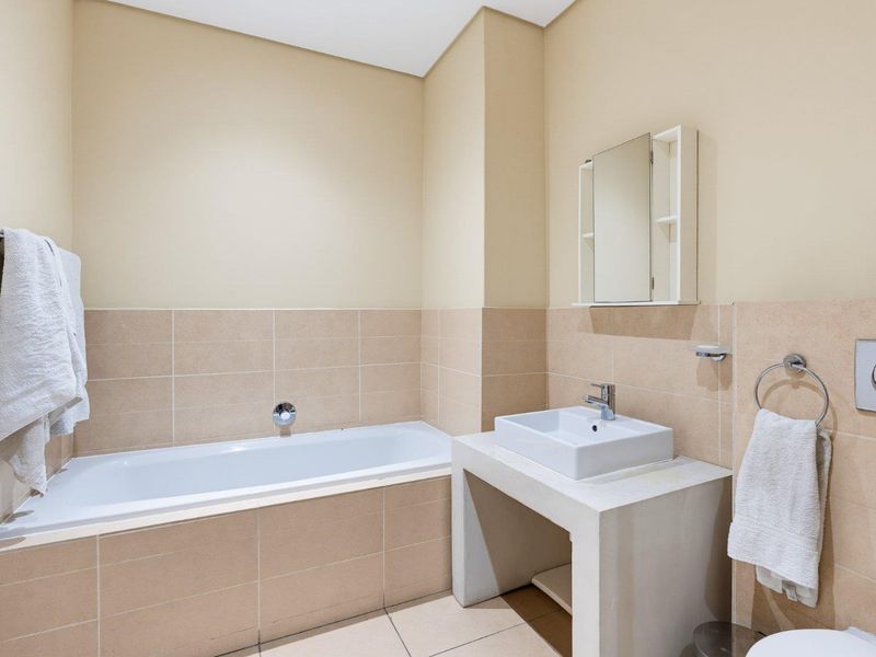 A clean, functional bathroom featuring a built-in bathtub, wall-mounted basin, and neutral tiled finishes, providing a practical and well-maintained space.