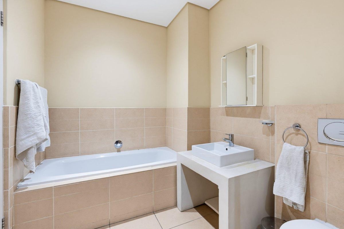 A clean, functional bathroom featuring a built-in bathtub, wall-mounted basin, and neutral tiled finishes, providing a practical and well-maintained space.