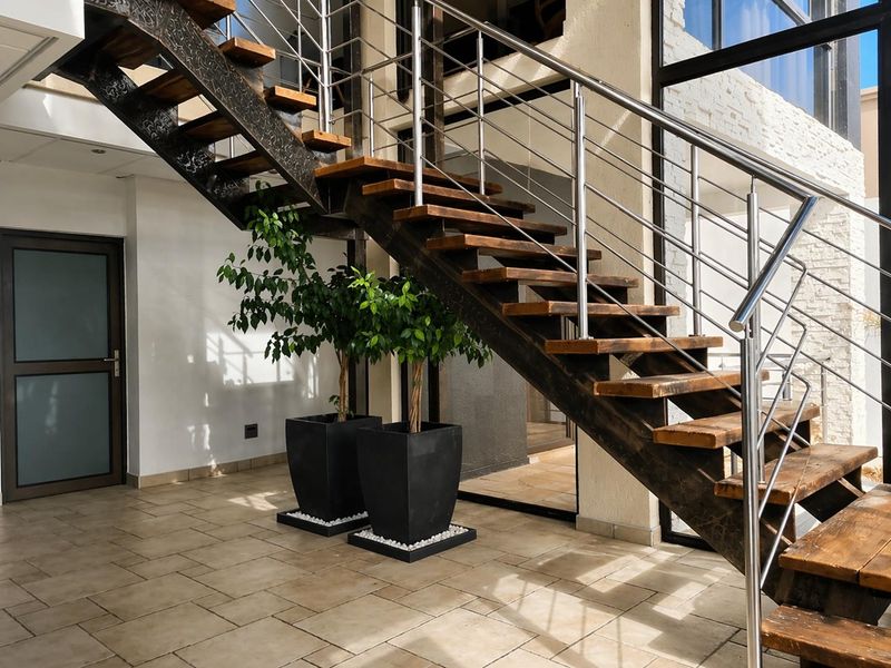 A bright and modern entrance hallway featuring a striking timber staircase with stainless steel balustrades and large windows providing ample natural light.