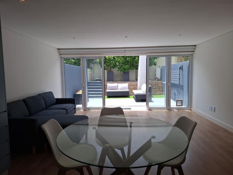 Open-plan living and dining area featuring modern laminate flooring, recessed lighting, and large sliding glass doors providing seamless access to the rear patio.
