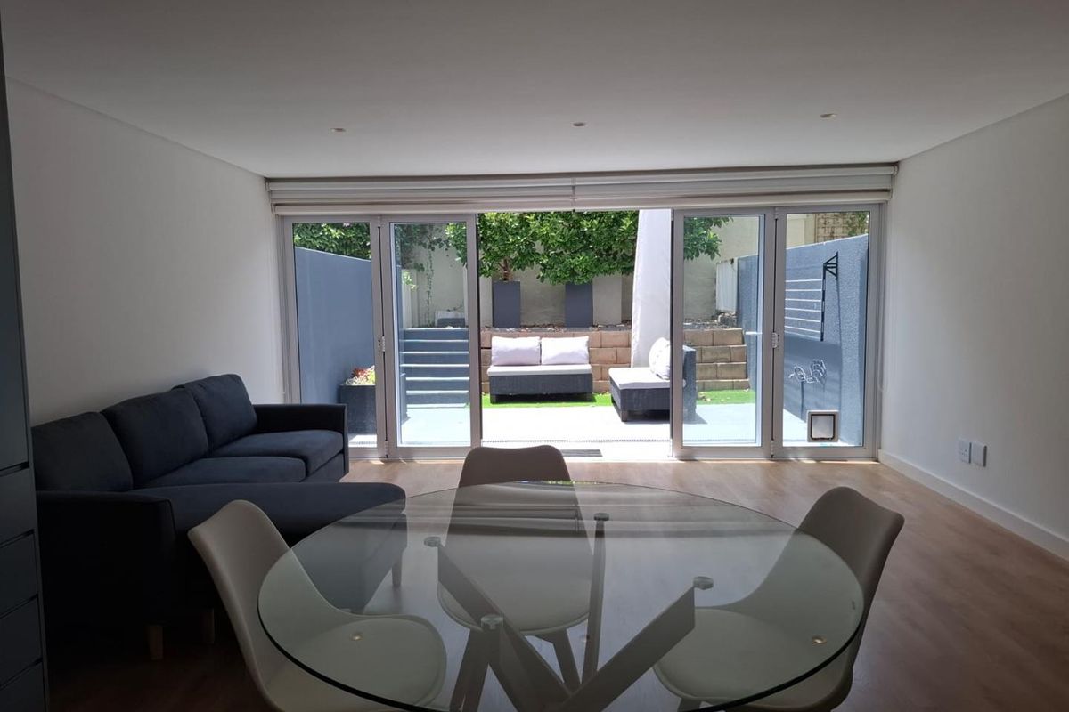 Open-plan living and dining area featuring modern laminate flooring, recessed lighting, and large sliding glass doors providing seamless access to the rear patio.