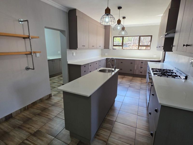 Modern kitchen featuring a central island, stone countertops, ample built-in cabinetry, gas hob, and tiled flooring, with an adjacent scullery area.