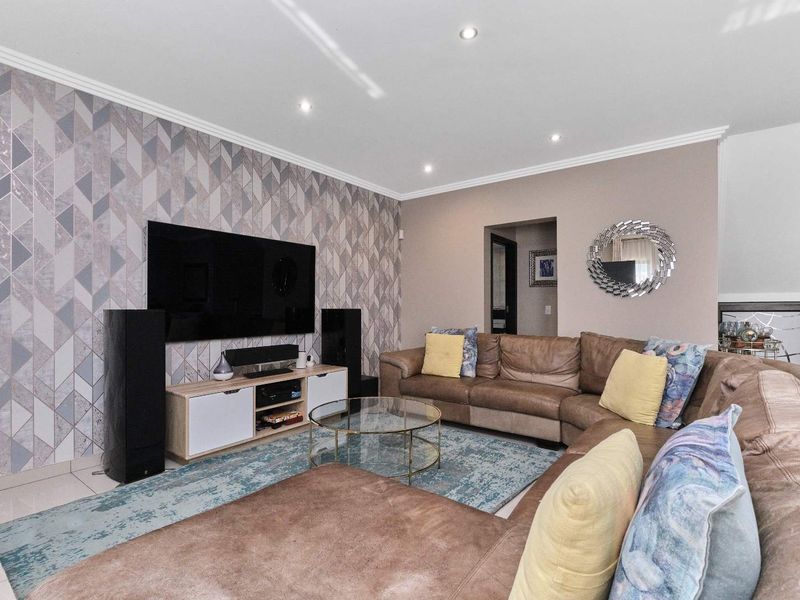 A well-maintained living room featuring modern recessed downlights, tiled flooring, and a decorative feature wallpaper wall.
