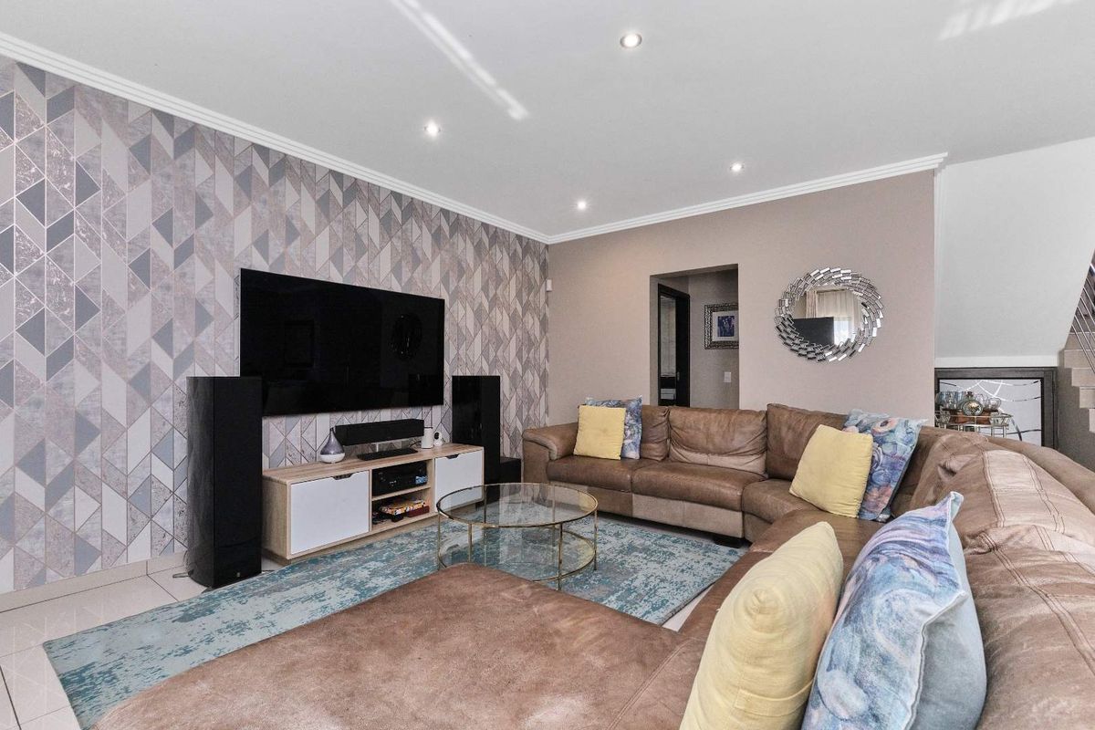 A well-maintained living room featuring modern recessed downlights, tiled flooring, and a decorative feature wallpaper wall.