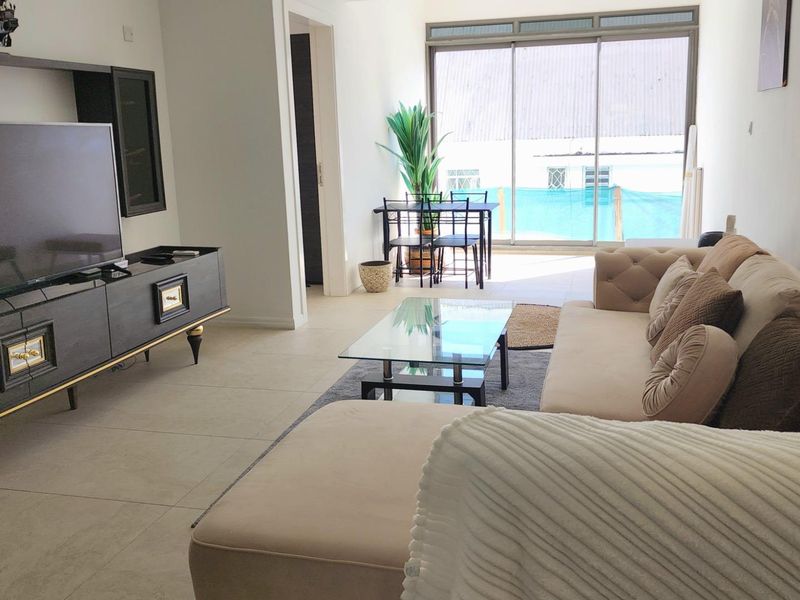 A bright living room featuring large sliding glass doors that open onto a balcony, with neutral tiled flooring and modern recessed lighting.