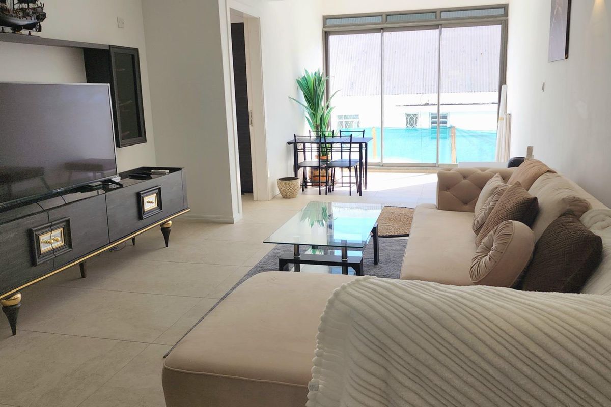 A bright living room featuring large sliding glass doors that open onto a balcony, with neutral tiled flooring and modern recessed lighting.