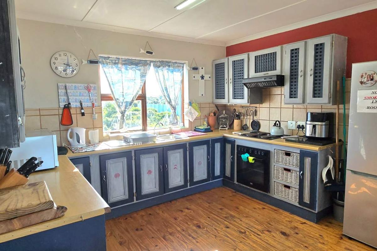 A functional kitchen featuring timber flooring, built-in cabinetry with laminate countertops, a built-in oven, hob, extractor fan, and a tiled backsplash.