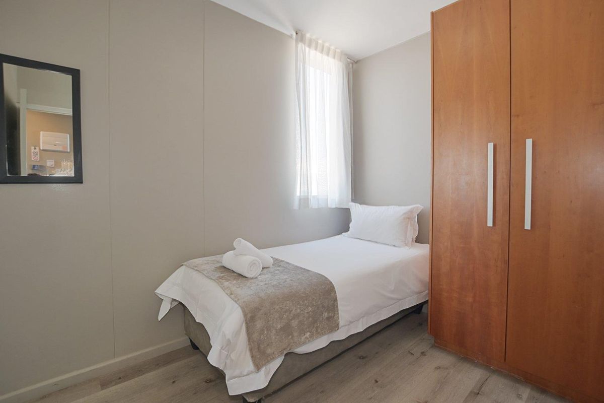 A compact bedroom featuring light wood-look flooring, neutral wall finishes, and a built-in wooden wardrobe.