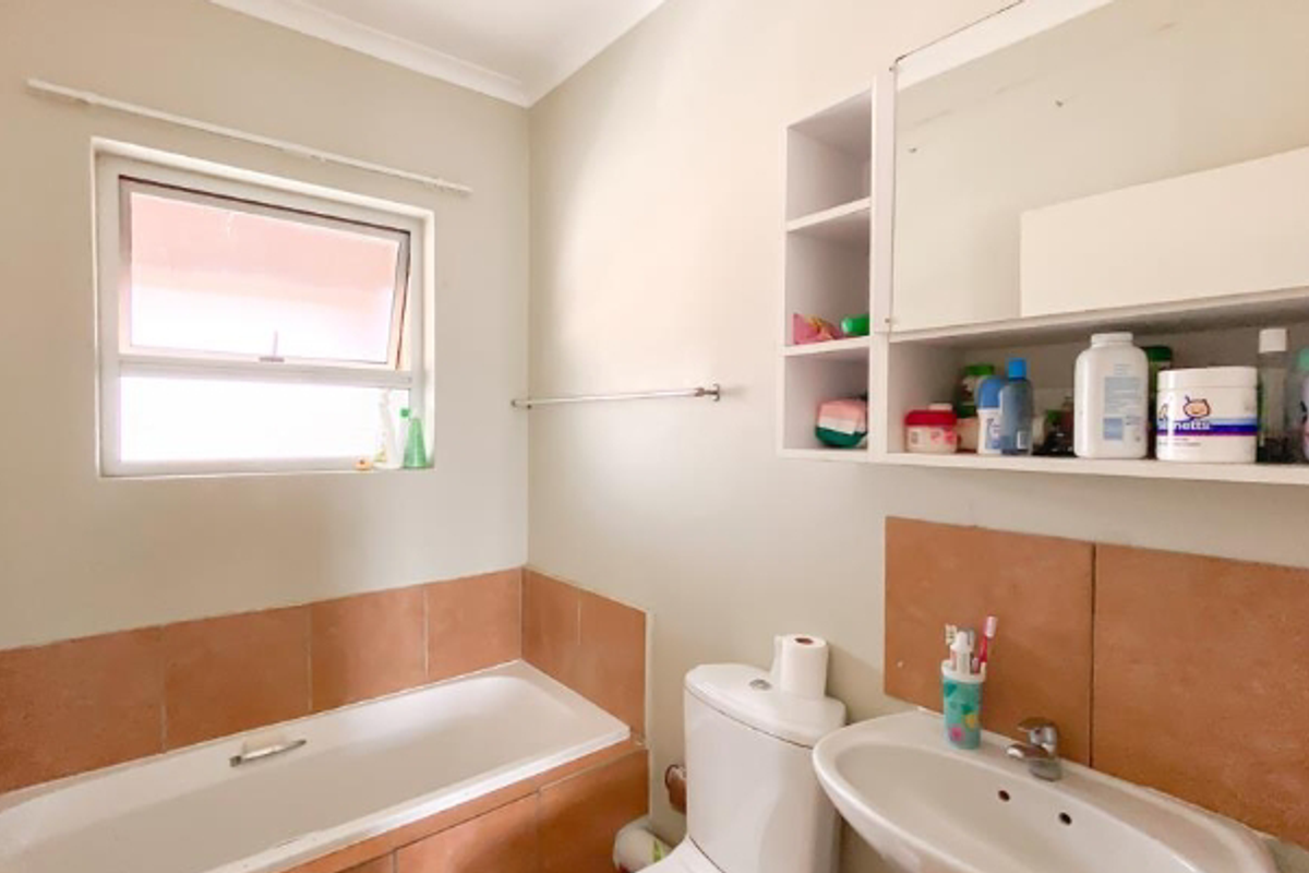 A functional bathroom featuring a built-in bathtub, pedestal sink, and wall-mounted storage cabinet with an integrated mirror.