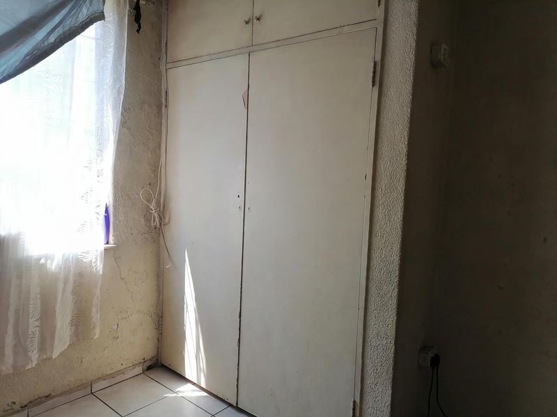 A bedroom featuring a built-in wardrobe and tiled flooring, currently in need of cosmetic repairs and wall surface restoration.
