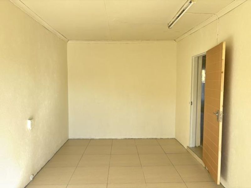An empty, tiled garage space featuring neutral walls, a single light fixture, and an internal access door.