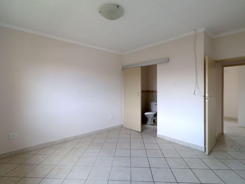 An empty bedroom featuring tiled flooring and an en-suite toilet accessed via a sliding door, with neutral wall finishes throughout.