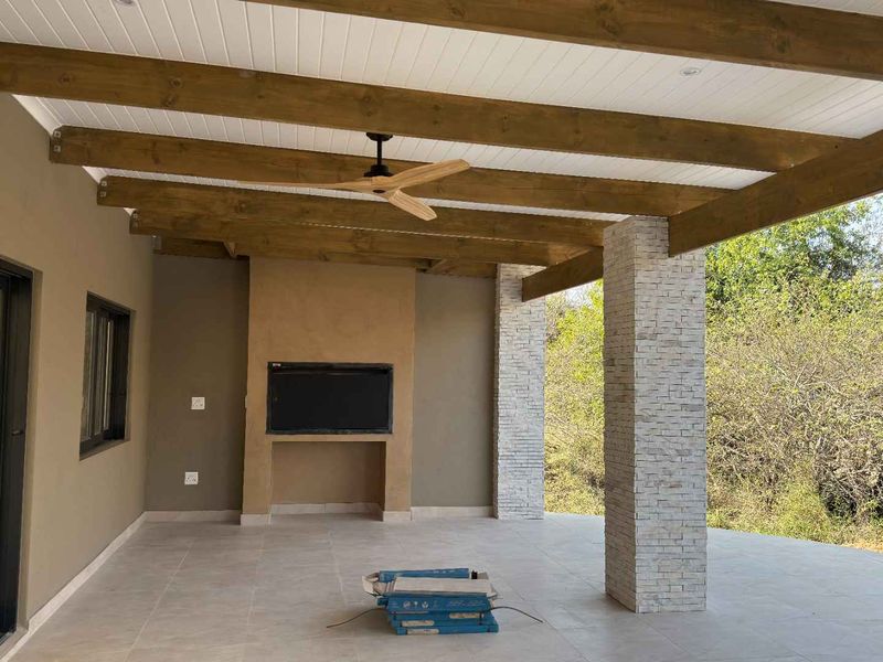 Spacious covered patio featuring exposed timber beams, stone-clad columns, and a built-in fireplace, offering a perfect space for outdoor entertaining.