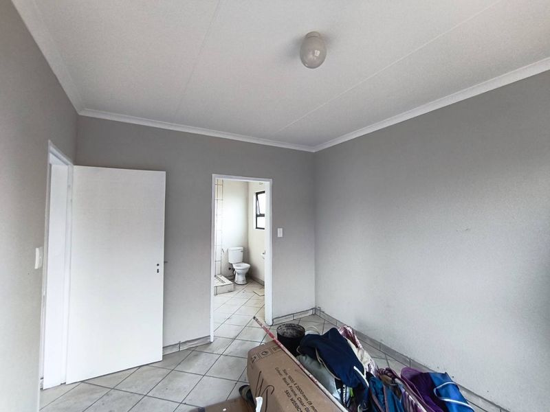 An empty bedroom featuring tiled flooring and neutral wall paint, with an adjacent view into a bathroom area.