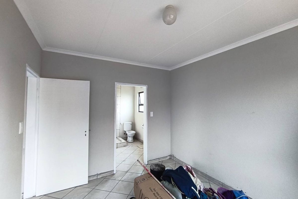 An empty bedroom featuring tiled flooring and neutral wall paint, with an adjacent view into a bathroom area.