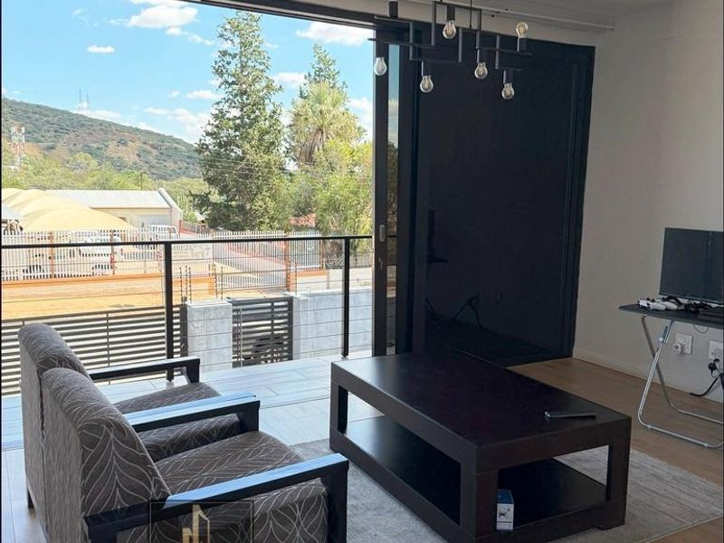 Bright living room featuring modern laminate flooring, recessed lighting, and large sliding glass doors opening onto a balcony with scenic views.