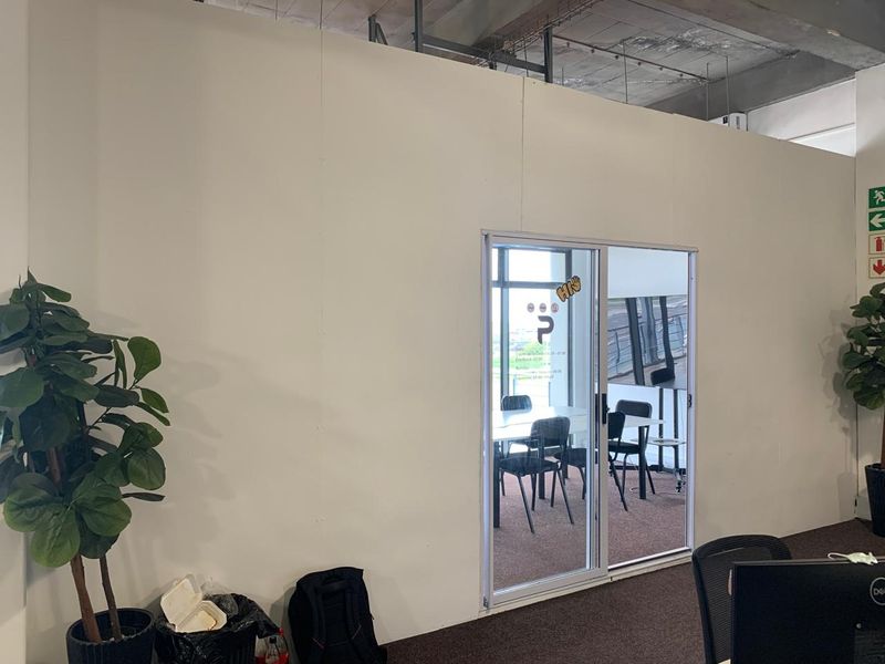 Office space featuring a sliding glass door partition, carpeted flooring, and an exposed industrial-style concrete ceiling.