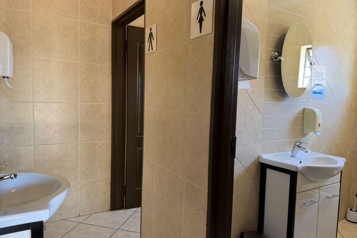 A clean, functional commercial restroom facility featuring tiled walls and floors, dual vanity units with basins, and wall-mounted fixtures.