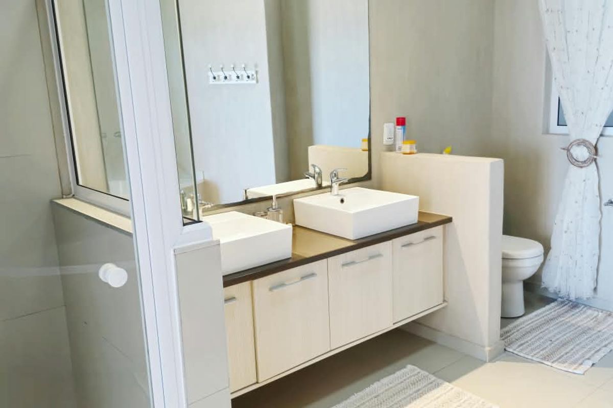 Modern bathroom featuring a double vanity with vessel sinks, a glass-enclosed shower, and neutral tiling throughout.