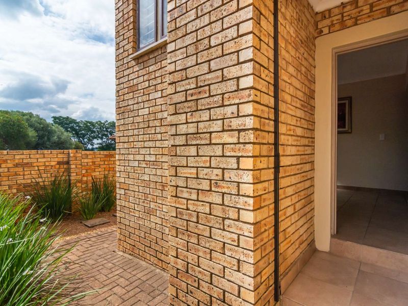 A view of the rear exterior featuring a face brick facade, paved patio area, and a brick boundary wall.