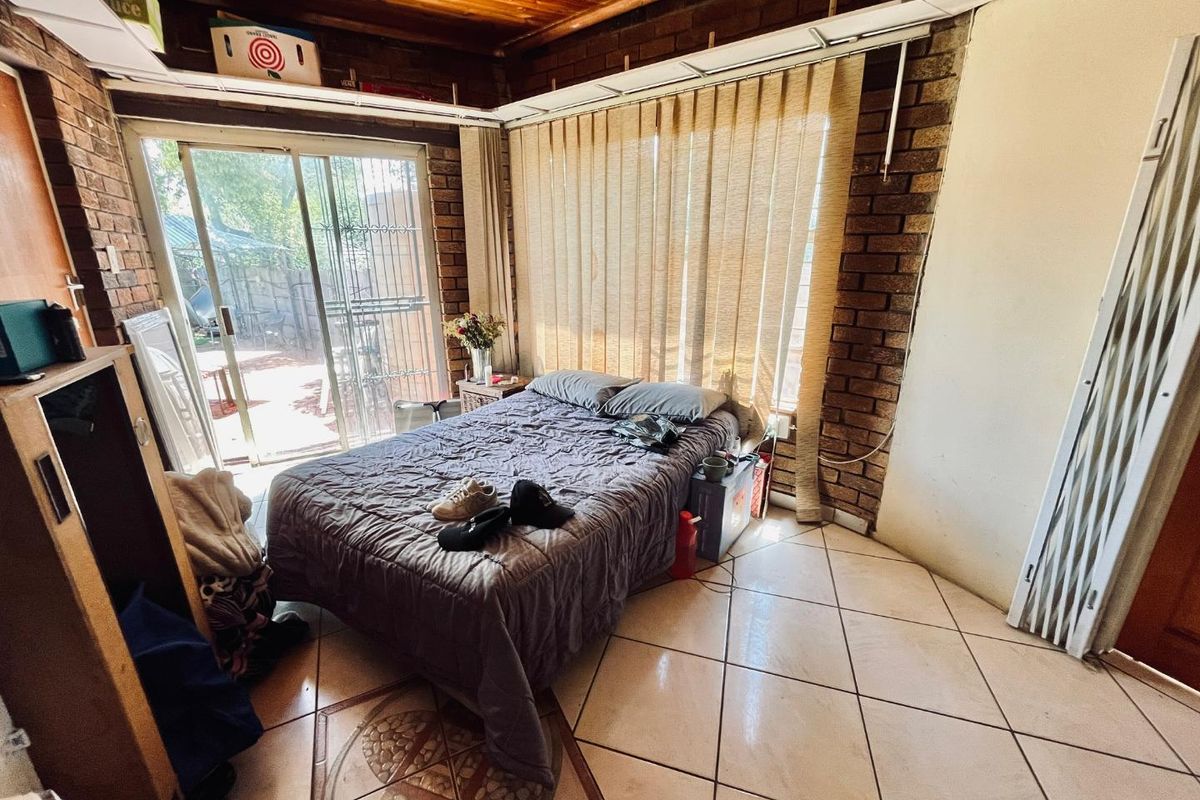 A bedroom featuring exposed timber ceiling beams, face-brick walls, tiled flooring, and sliding glass doors providing direct access to the outdoor area.