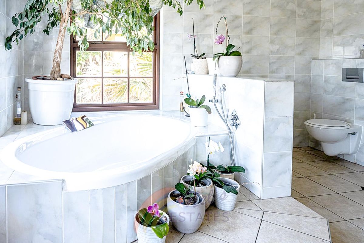 A spacious bathroom featuring a built-in oval bathtub, wall-mounted toilet, and tiled finishes throughout.