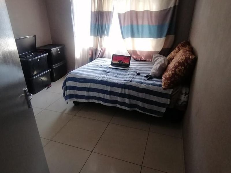 A standard bedroom featuring tiled flooring and a window with a curtain rod, providing a functional living space.