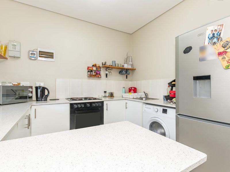 Compact kitchen featuring white cabinetry, stone-look countertops, a built-in oven and hob, and an integrated washing machine.