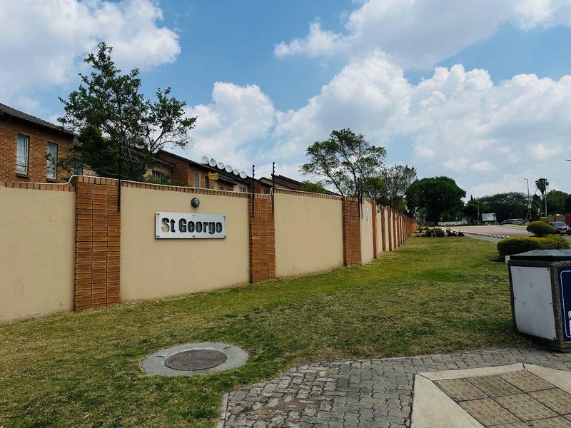 Street view of the St George apartment complex, featuring a secure perimeter wall with electric fencing and well-maintained surrounding grounds.