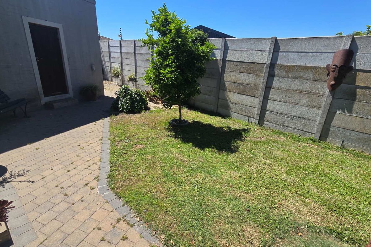 A rear garden area featuring a paved patio, a small lawn, and a precast concrete boundary wall.