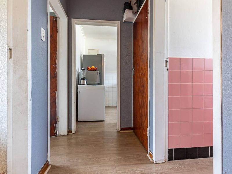 A functional hallway featuring laminate flooring and vintage pink wall tiles, providing access to adjacent rooms within the apartment.