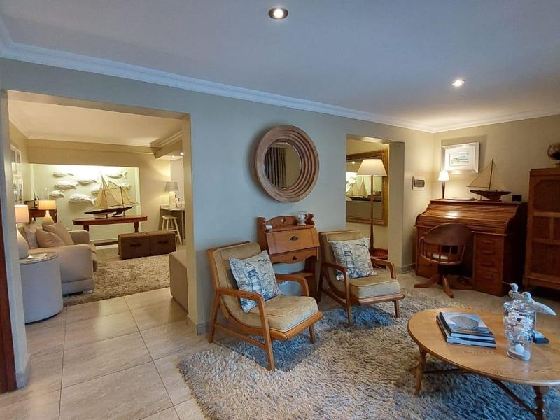 A spacious living area featuring tiled flooring, recessed downlighting, and coved cornicing, with an open-plan flow into an adjacent secondary living space.