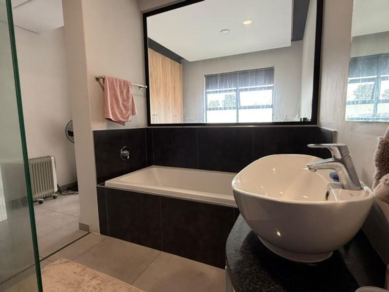 Modern bathroom featuring a vessel sink, built-in bathtub with dark tile surround, and a glass-enclosed shower area.
