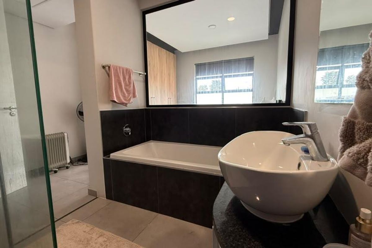 Modern bathroom featuring a vessel sink, built-in bathtub with dark tile surround, and a glass-enclosed shower area.