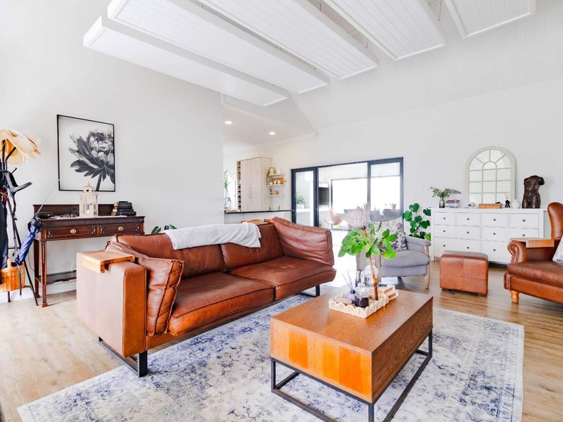 Spacious open-plan living area featuring vaulted ceilings with exposed beams, light laminate flooring, and large sliding glass doors leading to an outdoor space.
