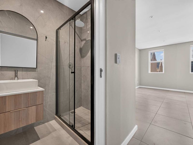 Modern bathroom featuring a wall-mounted vanity with vessel sink and a glass-enclosed shower with black fixtures, adjacent to an open-plan living area.