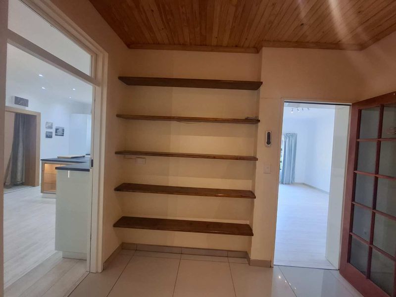 A bright hallway featuring built-in wooden shelving, tiled flooring, and a timber ceiling, providing access to adjacent living and kitchen areas.