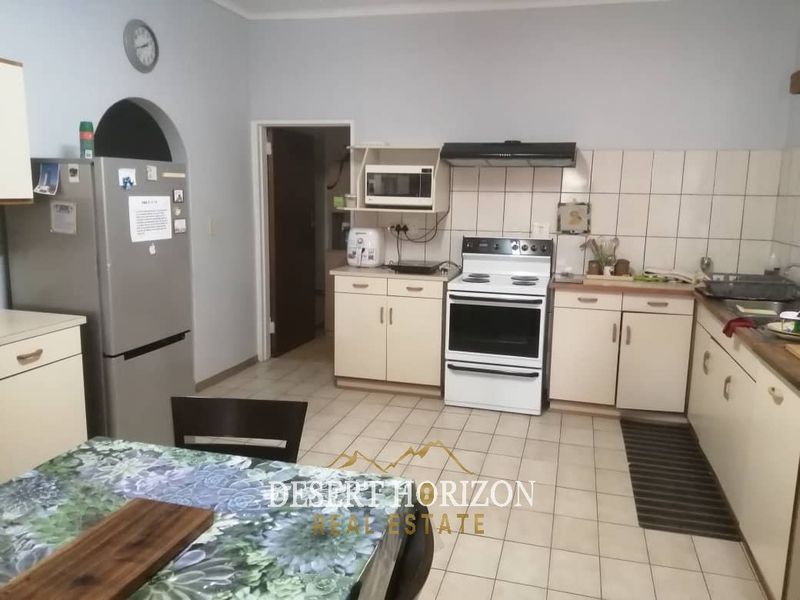 A functional kitchen featuring built-in cabinetry, a tiled backsplash, and a freestanding electric stove with an overhead extractor fan.