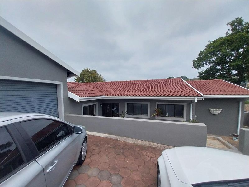Front elevation of a cottage featuring a tiled roof, grey exterior walls, aluminium window frames, and a paved driveway with an attached garage.